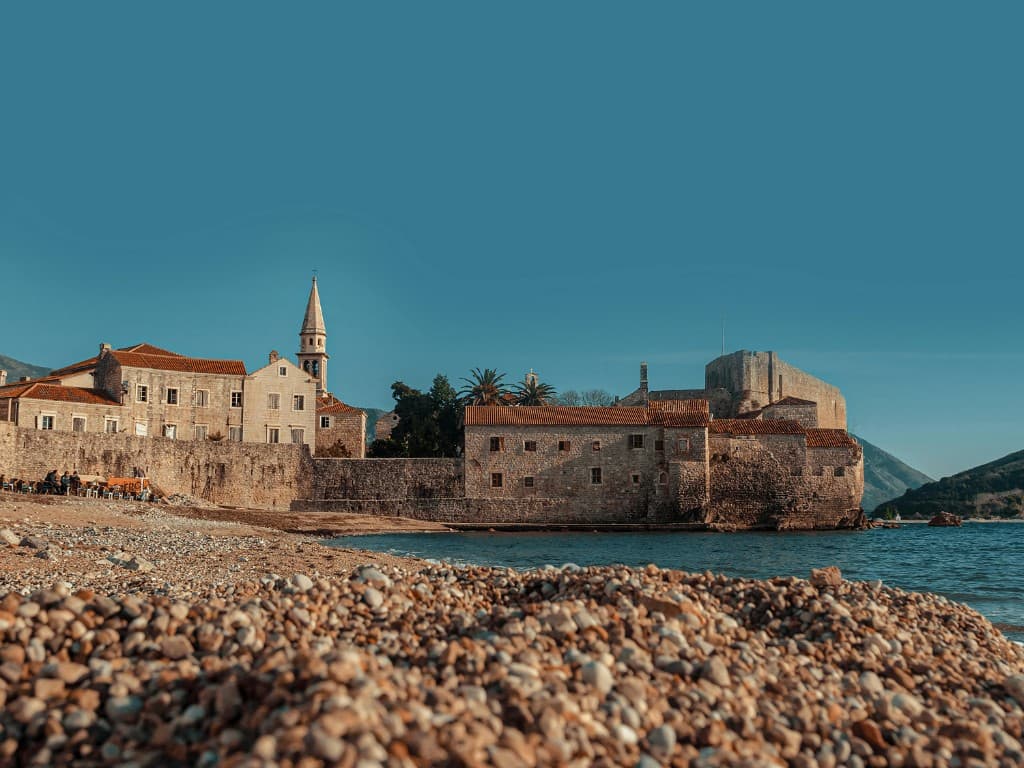 Korčula old town on the water: stone walls, terracotta roofs, church spire above a pebble beach and calm Adriatic sea