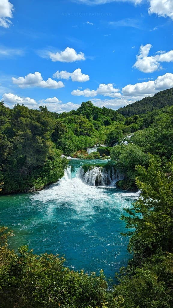 Krka waterfalls, turquoise pools and cascades through lush forest under a bright blue sky in Croatia