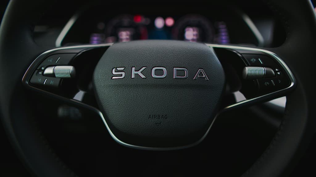 Škoda steering wheel hub with metallic branding and driver controls, digital cockpit softly blurred behind